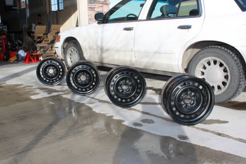 1998 Ford Crown Victoria - Four black steel wheels are lined up in front of a white sedan in a garage.