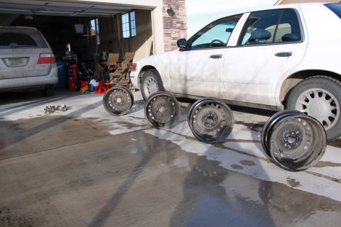 1998 Ford Crown Victoria - A white 1998 Ford Crown Victoria is parked next to four steel wheels in a garage.