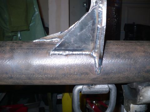 1979 Ford Bronco - A close-up view of a welded metal bracket on a pipe, with a U-shaped clamp visible underneath.