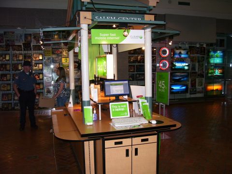 1991 Ford Bronco - A retail kiosk displays electronics and promotional materials, with two individuals present.