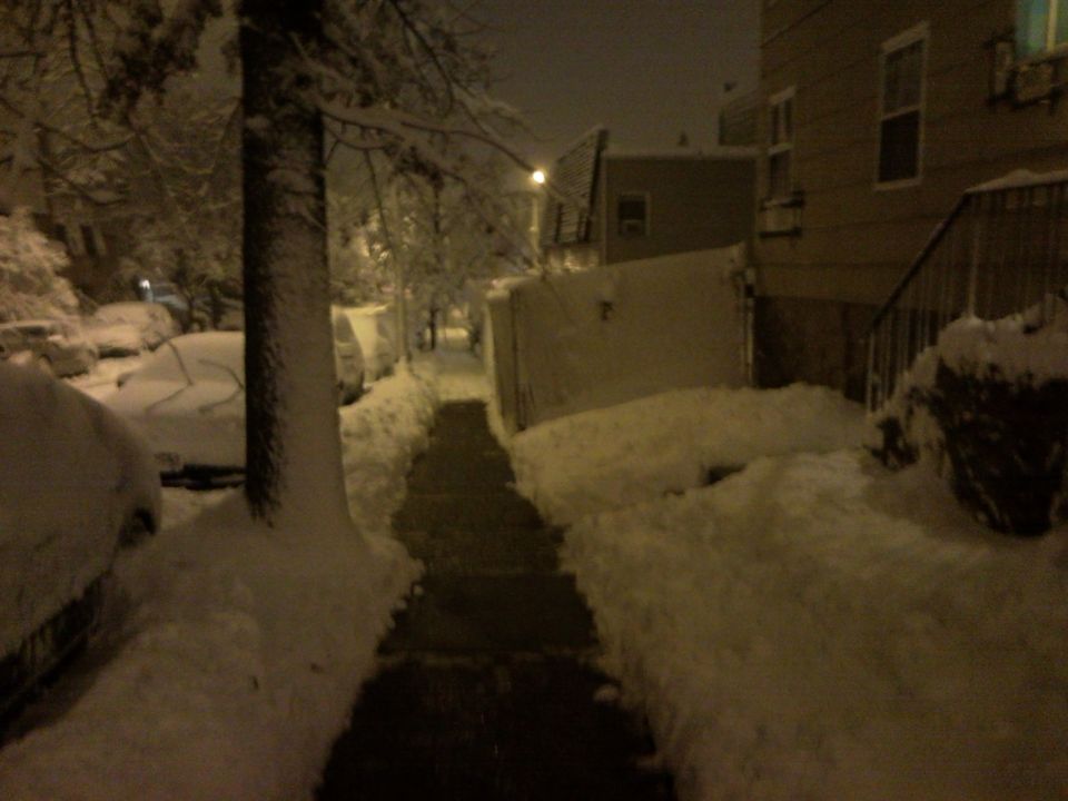 Snow-covered cars parked on a street during a snowstorm
