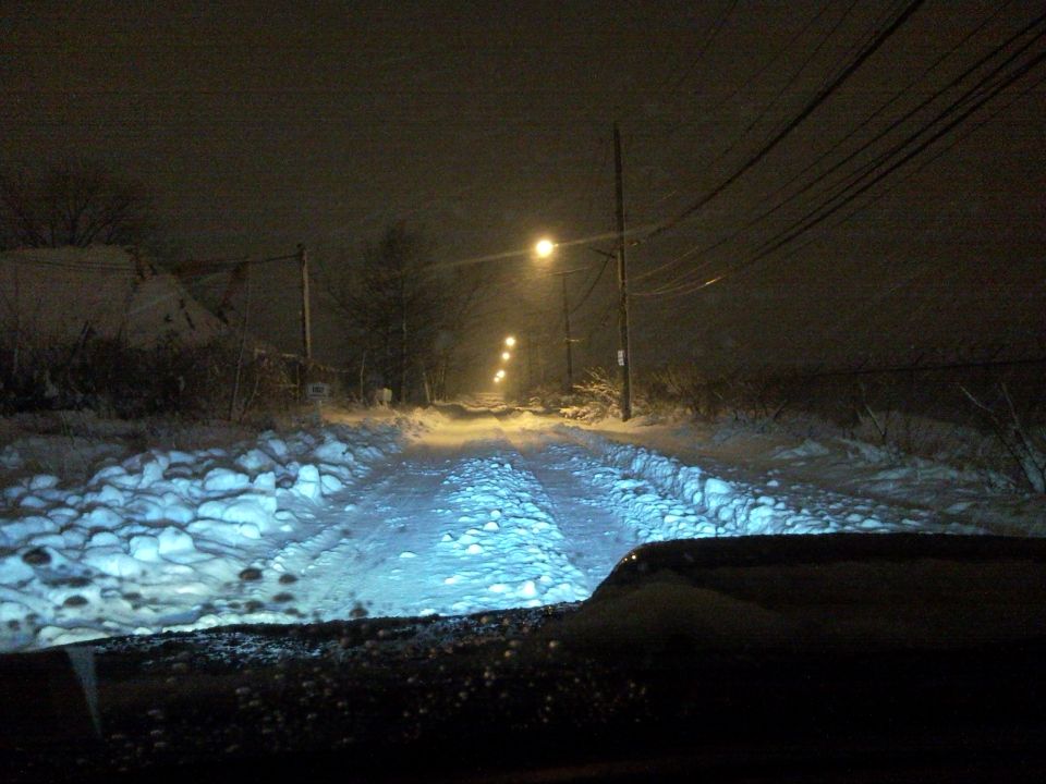 View from inside a vehicle looking out at a dark, snowy road with streetlights