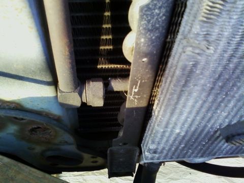 1990 Ford Bronco - The radiator and associated plumbing are shown in this close-up view, with some corrosion evident on the metal components.