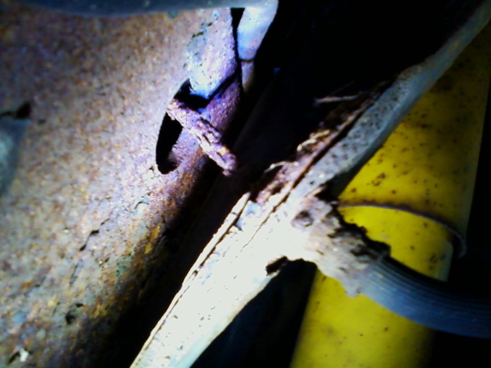 Close-up of heavily rusted metal frame with a yellow shock absorber and black hose