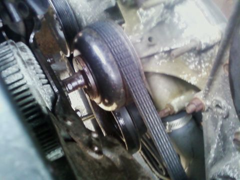 1990 Ford Bronco - Close-up view of an engine's belt and pulley system, showing mechanical components and a water hose.
