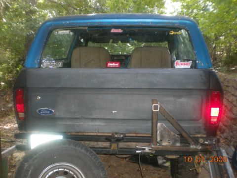 1979 Ford Bronco - Rear view of a blue and gray Ford Bronco, showing the tailgate and taillights, with various stickers on the rear window.