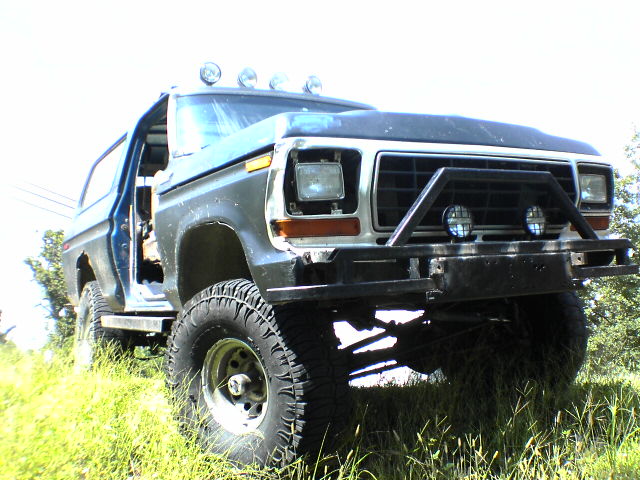 Gray Ford Bronco with off-road tires and a brush guard, parked on a grassy incline