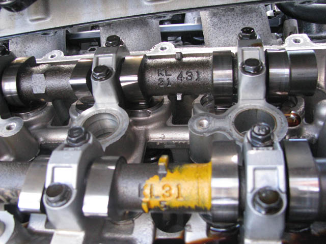 Close-up of camshafts in a cylinder head with KL 431 and KL31 casting marks, one marked in yellow paint