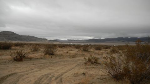 1997 Ford Ranger - A wide shot of a desert landscape with tire tracks in the foreground and mountains in the distance under a cloudy sky.