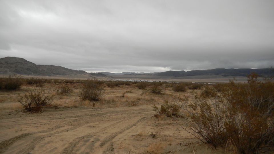 Desert landscape with tire tracks under a cloudy sky. Supermotors.net logo in corner