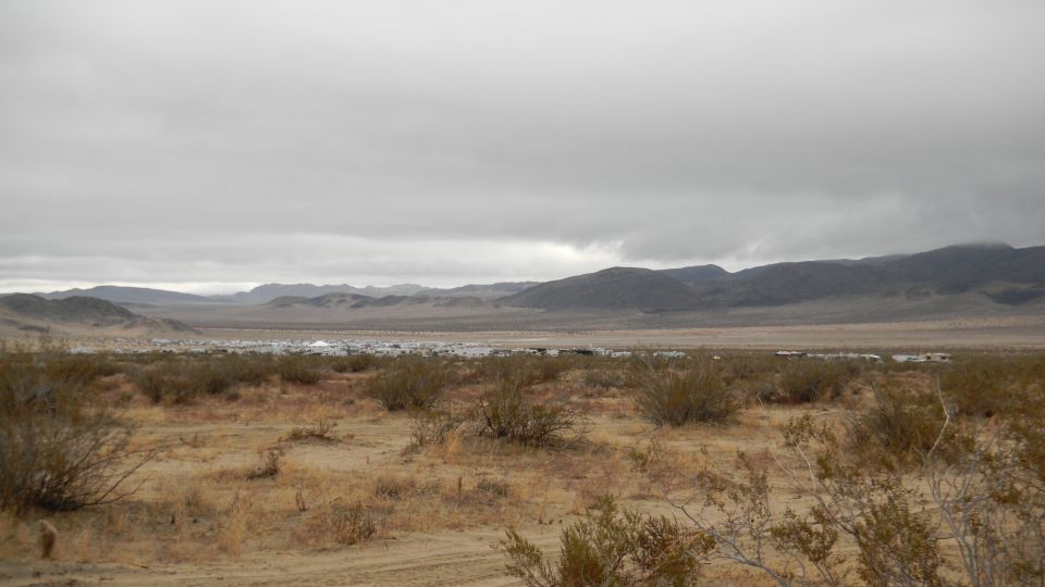 Desert landscape with distant vehicles parked in a valley under a cloudy sky