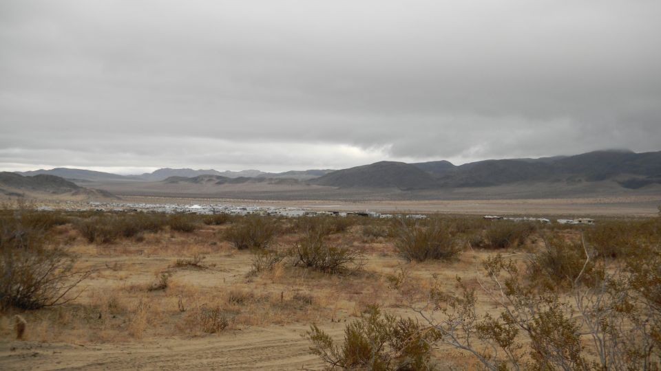 Desert scene with distant vehicles and mountains under a cloudy sky. Supermotors.net logo in corner