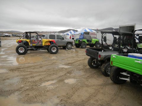1997 Ford Ranger - Several off-road vehicles and a pickup truck are parked in a muddy lot with tents in the background.