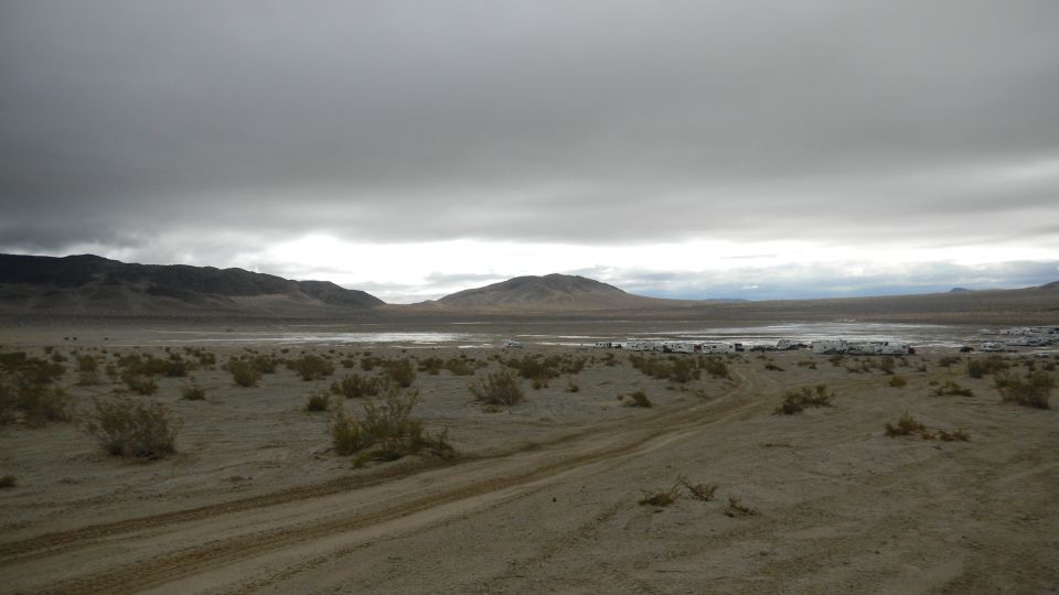 Desert scene with distant vehicles under cloudy sky