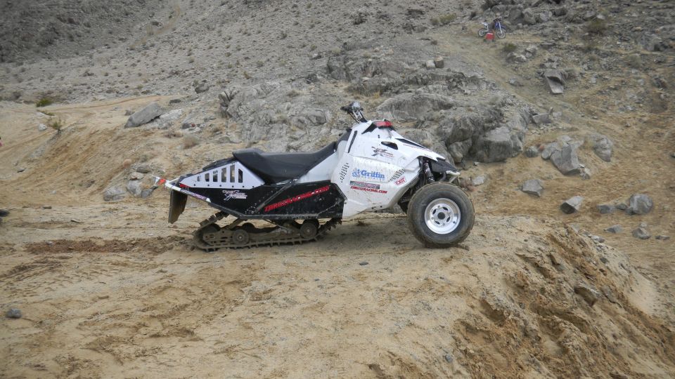 White ATV with tracks on rear, driving on a dirt hill