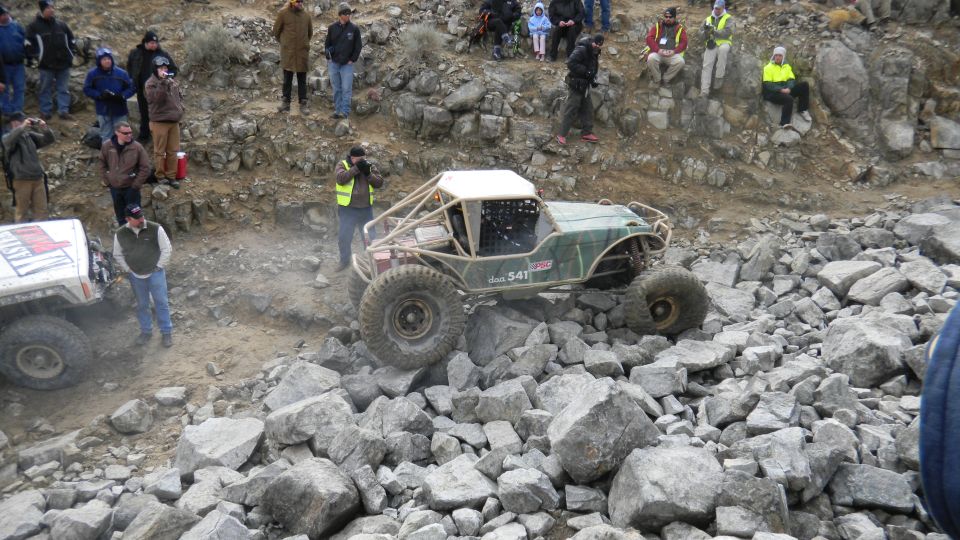 Off-road buggy with roll cage climbing over rocks, another vehicle to the left