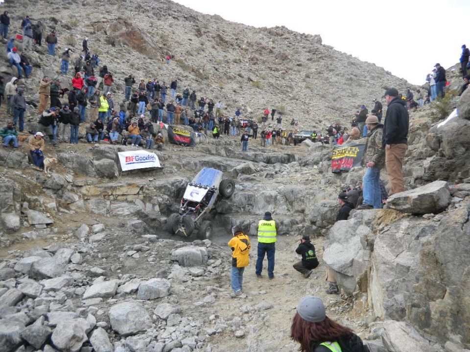 Off-road vehicle climbing a rocky hill with spectators watching. BFGoodrich banner visible