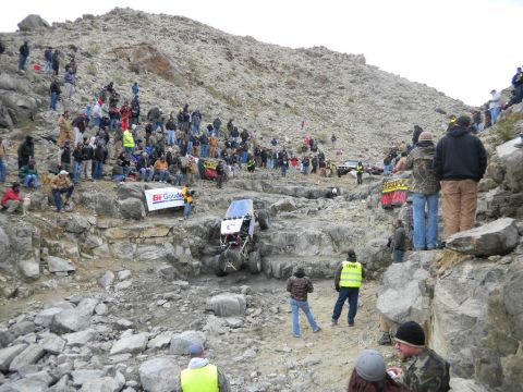 1997 Ford Ranger - A tube-chassis rock buggy climbs a near-vertical rocky ledge on a desert hillside while a large crowd of spectators watches from the rocks…