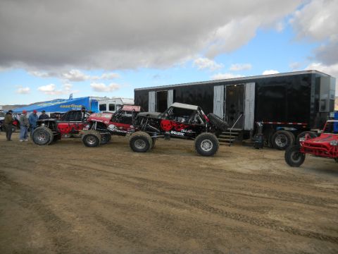 1997 Ford Ranger - Multiple custom off-road vehicles are lined up next to a large trailer under a cloudy sky.