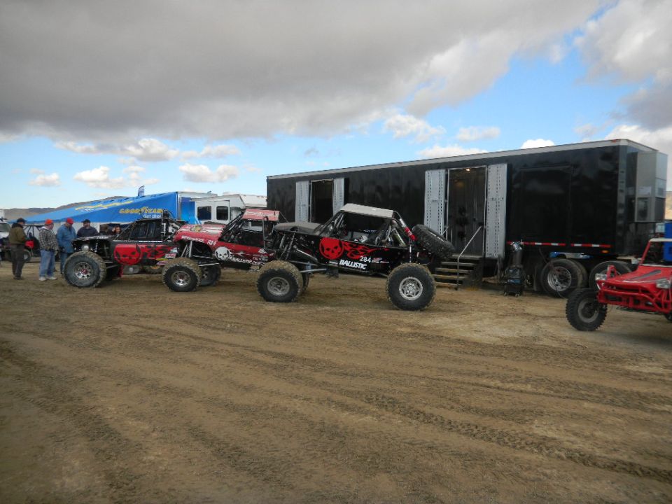 Several off-road buggies parked in front of a large black trailer