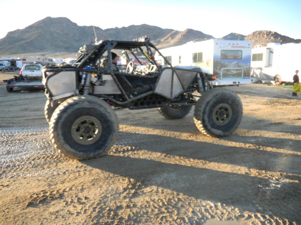 Buggy with big tires parked on dirt, RVs in background
