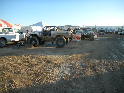1997 Ford Ranger - Multiple off-road vehicles and support trucks are parked in a dusty lot under a clear sky.