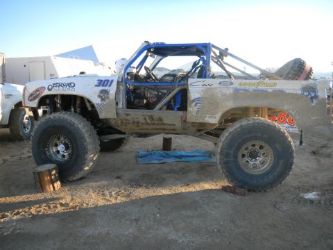 1997 Ford Ranger - Modified off-road truck with extensive roll cage and large tires sits on dirt terrain.