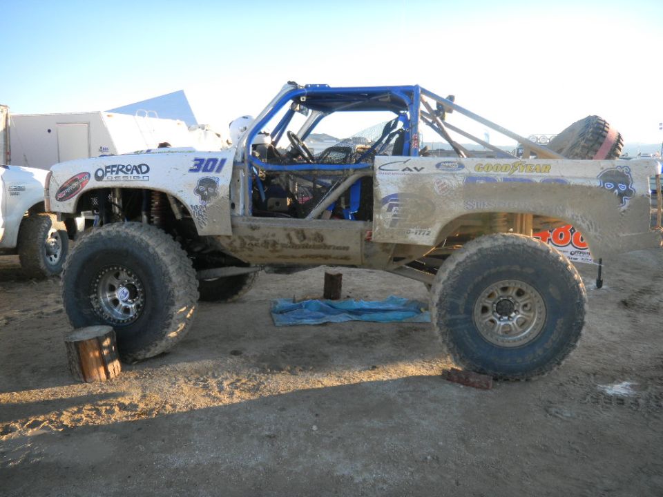 Modified off-road truck with roll cage, number 301, and Goodyear tires. Another vehicle is partially visible to the left