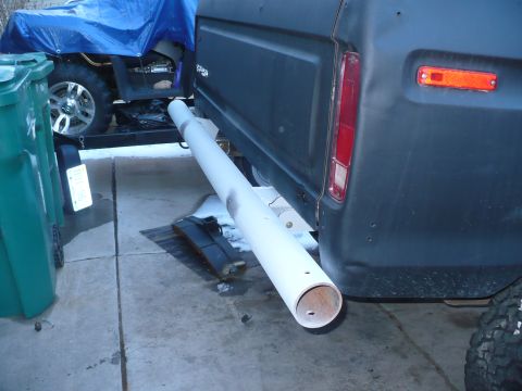 1979 Ford Bronco - A large white pipe is attached to the rear bumper of a dark SUV, obscuring the vehicle's year and model.