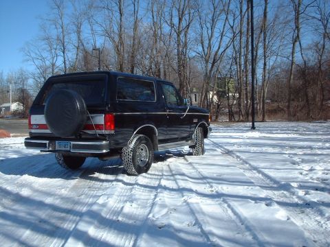 1989 Ford Bronco - A black Ford Bronco sits in a snowy lot with trees in the background.