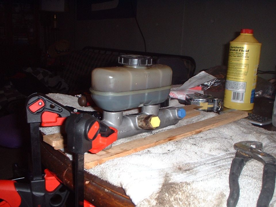 Brake master cylinder with reservoir and yellow cap, next to a bottle of brake fluid