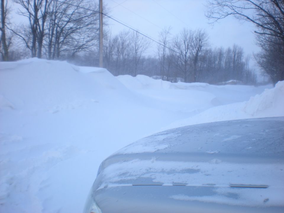 Silver vehicle hood covered in snow, driving through a snow-covered landscape