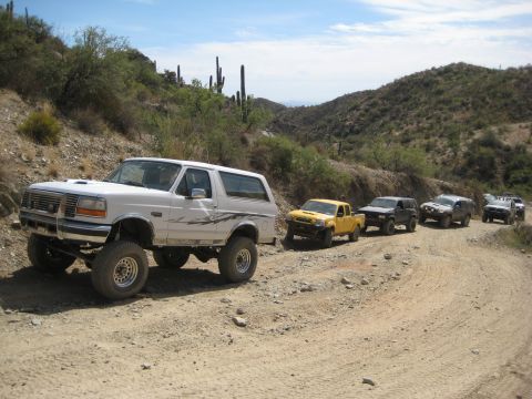 1996 Ford Bronco - A convoy of off-road vehicles navigates a desert trail under a clear blue sky.
