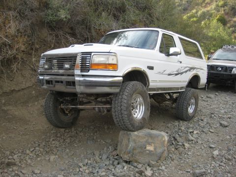 1996 Ford Bronco - A white Ford Bronco navigates a rocky off-road path, with another vehicle visible behind it.