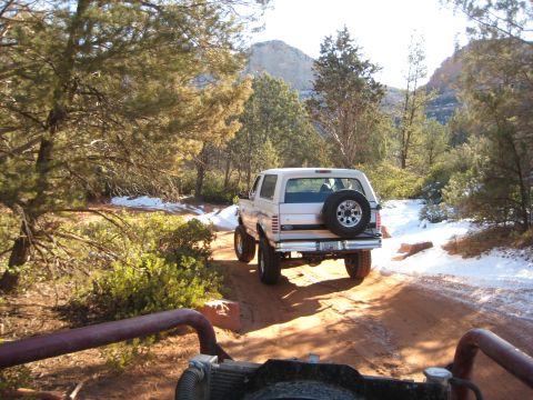 1996 Ford Bronco - A white 1996 Ford Bronco navigates a snowy dirt road in a mountainous, wooded area.