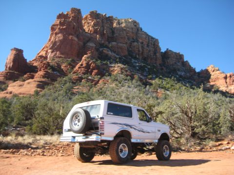1996 Ford Bronco - A lifted 1996 Ford Bronco is parked in a desert landscape with large red rock formations behind it.