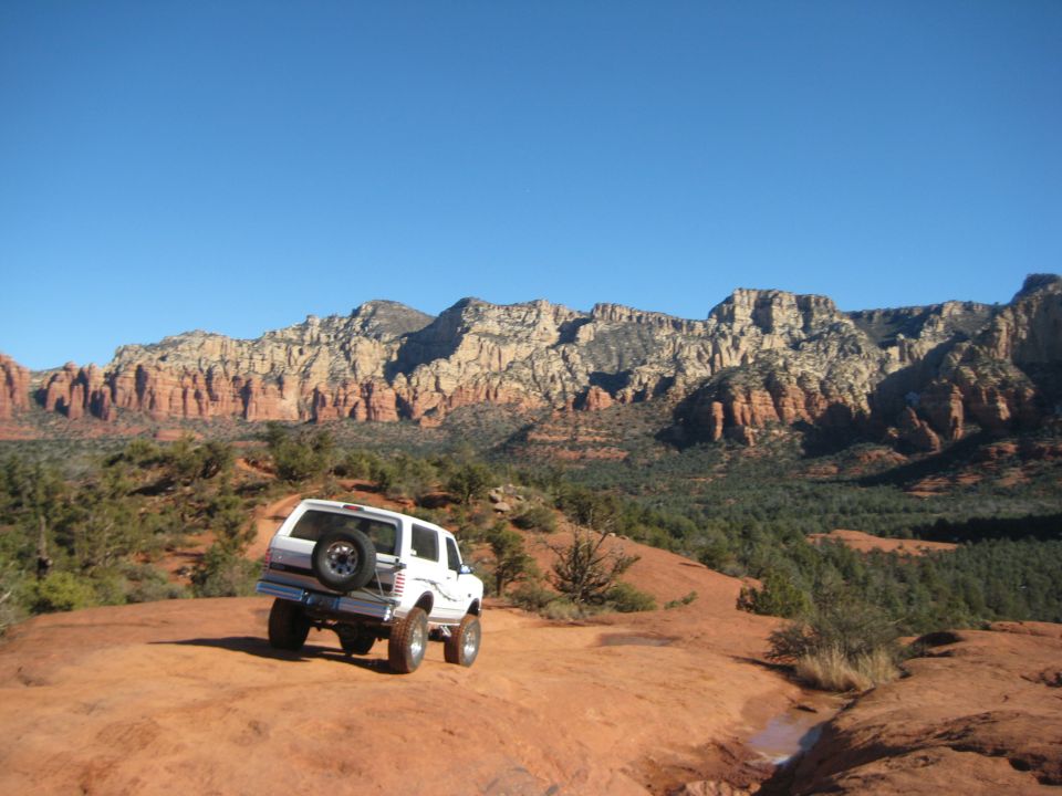 White 1996 Ford Bronco parked on a red rock trail with mountains in the background