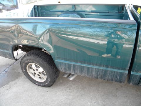 1995 GMC Sierra 1500 - The rear passenger side of a green pickup truck shows extensive damage to the body panels.