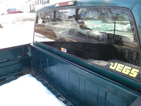 1995 GMC Sierra 1500 - A green pickup truck is parked in the snow, with a reflection of another vehicle visible in its rear window.