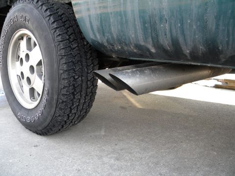 1995 GMC Sierra 1500 - Close-up of the dual exhaust pipes and rear tire of a green truck, showing Firestone Destination A/T tires.