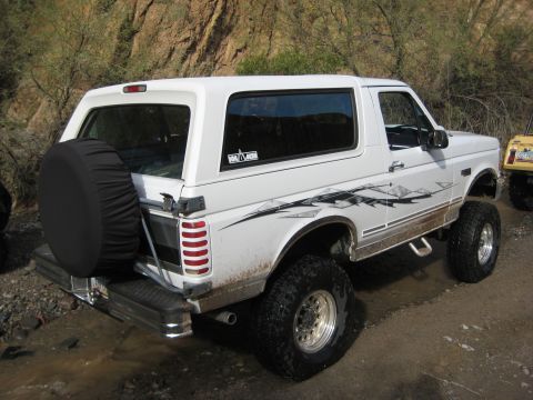 1996 Ford Bronco - White Ford Bronco with custom graphics and lifted suspension is parked off-road.