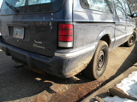 1993 Dodge Grand Caravan - The rear of a blue minivan is shown, covered in dirt and mud, with a visible license plate.