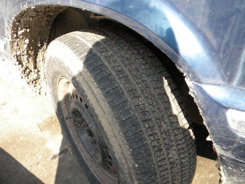 1993 Dodge Grand Caravan - Mud cakes the wheel well and tire of a blue vehicle, obscuring details of its make and model.