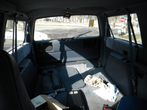 1993 Dodge Grand Caravan - Rear interior view of a minivan with a cluttered cargo area and a view of the street through the back window.