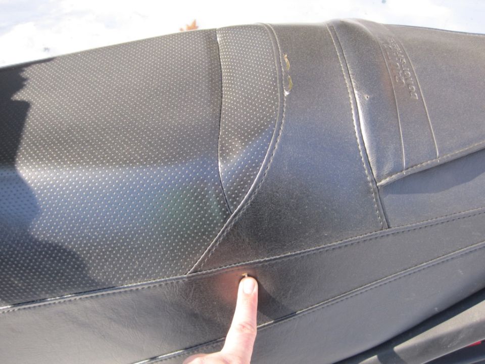 Finger pointing to seam damage on a black snowmobile vinyl seat