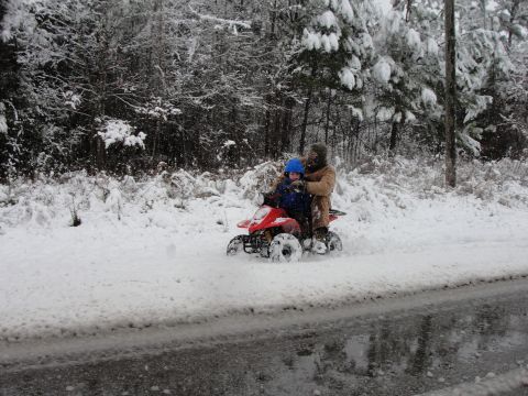1967 Ford Mustang - Two people ride a red ATV through a snowy wooded area.