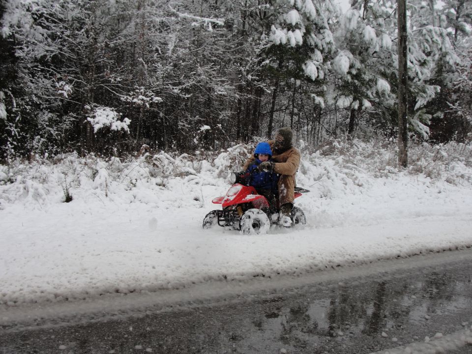 Two people ride a red ATV through a snowy wooded area