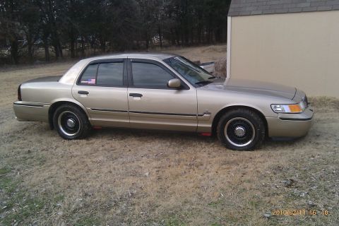 2000 Mercury Grand Marquis - Side view of a 2000 Mercury Grand Marquis sedan parked outdoors on a dry, grassy area.