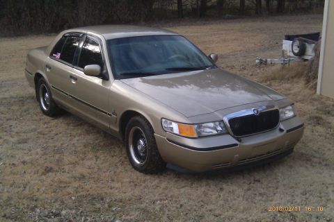 2000 Mercury Grand Marquis - This Mercury Grand Marquis is parked on a dry, grassy area with a trailer visible in the background.