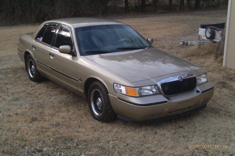 Front view of a gold Mercury Grand Marquis sedan parked on dry grass